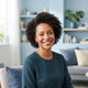 A professional portrait of a smiling woman in a bright, modern room with soft blue accents, looking healthy and relaxed.